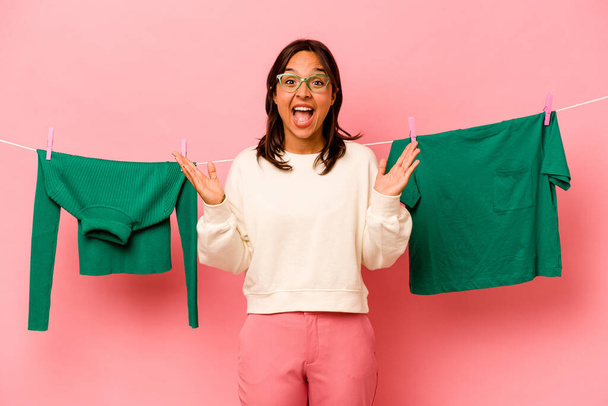 Junge hispanische Frau hält Wäschekorb isoliert auf rosa Hintergrund eine angenehme Überraschung, aufgeregt und hebt die Hände. - Foto, Bild