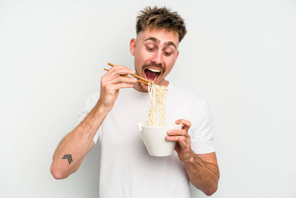Young caucasian man eating noodles isolated on white background - 写真・画像