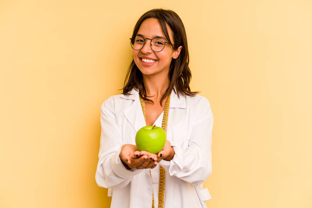 Young nutritionist woman holding a weighing machine isolated on yellow background - Photo, Image