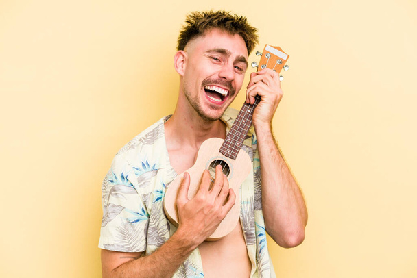 Young caucasian holding a ukulele isolated on yellow background - Zdjęcie, obraz