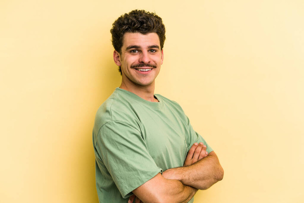 Young caucasian man isolated on yellow background who feels confident, crossing arms with determination. - Photo, Image
