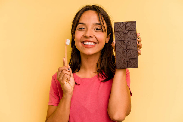 Young hispanic woman washing teeth after eating chocolate isolated on yellow background - Foto, Imagem
