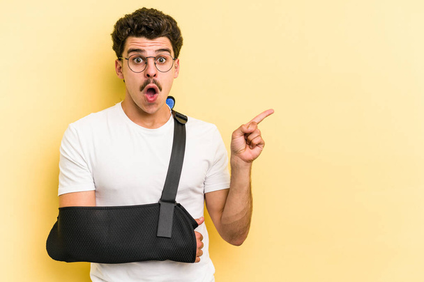 Young caucasian man with broke hand isolated on yellow background pointing to the side - Photo, image