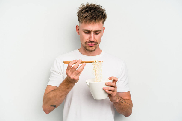 Young caucasian man eating noodles isolated on white background - 写真・画像