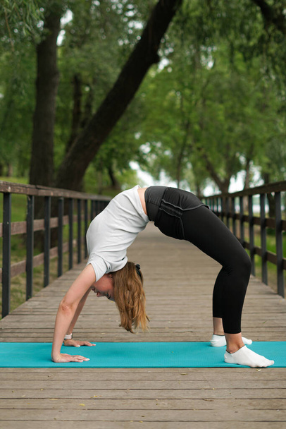 meisje gaat naar binnen voor sport, doet stretching in het park op de brug - Foto, afbeelding