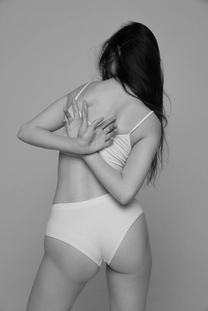 Portrait of young girl with slim back, tender figure posing in white underwear. Black and white photography aesthetics. Concept of natural beauty, body and skin care, femininity, self-acceptance, ad - 写真・画像