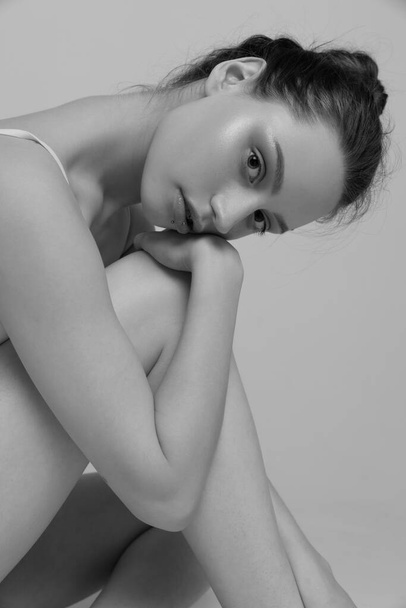 Retrato de jovem mulher sentada, posando. Estética da fotografia em preto e branco. Olhar atento. Conceito de beleza natural, cuidados com o corpo e a pele, feminilidade, auto-aceitação, ad - Foto, Imagem