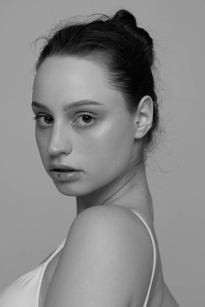 Portrait of young beautiful girl with no makeup posing, looking at camera. Black and white photography. Concept of natural beauty, body and skin care, femininity, self-acceptance, ad - Фото, изображение