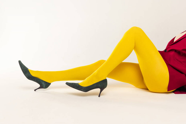 Immagine ritagliata di gambe femminili in collant giallo brillante e tacchi isolati su sfondo grigio studio. Moda straordinaria. Concetto di moda retrò, fotografia d'arte, stile, queer, bellezza - Foto, immagini