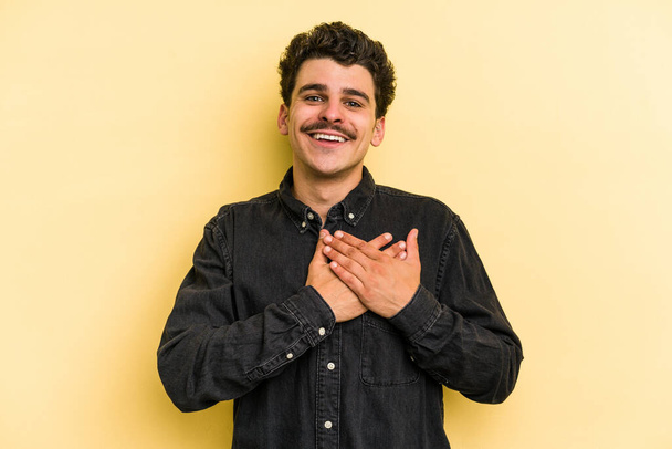 Young caucasian man isolated on yellow background has friendly expression, pressing palm to chest. Love concept. - Photo, Image
