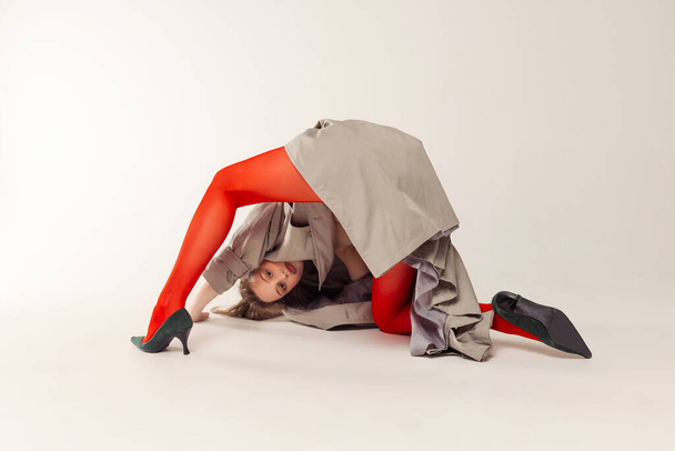 Portrait of young woman in red tights, jacket and heels posing isolated over grey studio background. Doing a somersault. Concept of retro fashion, art photography, style, queer, beauty - Fotoğraf, Görsel