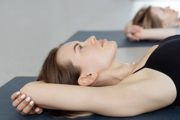 Slim young woman lying in Supta Virasana, reclining Hero Pose, stretching abdominal and back muscles on mat in gym.  - Photo, Image
