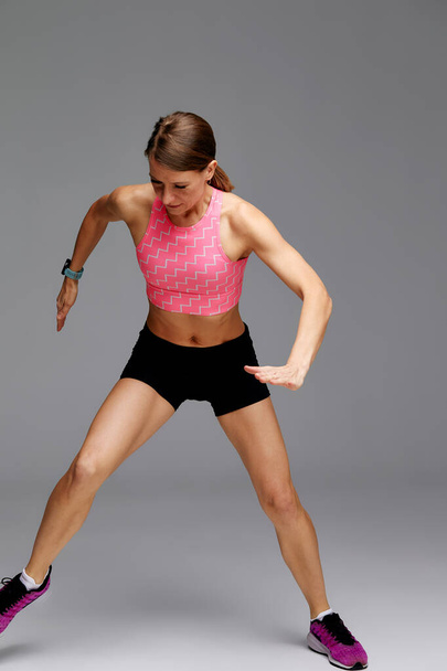 Fitness woman jumping and running, working out. Athletic girl doing jump in studio on gray background. - Fotó, kép