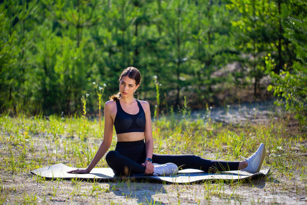 Young athletic slim girl in a black leotard does gymnastics or yoga in the forest - Photo, Image