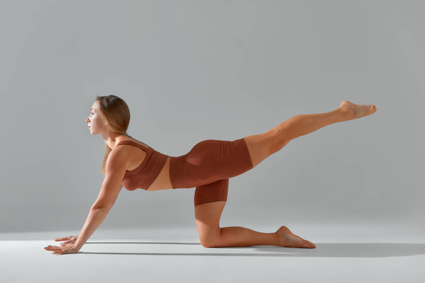 Yoga, pilates, sport and fitness concept: fit woman in biege leggings and top working out, warming up or doing exercise. Sporty woman sitting on yoga mat and looking ahead. - Photo, image