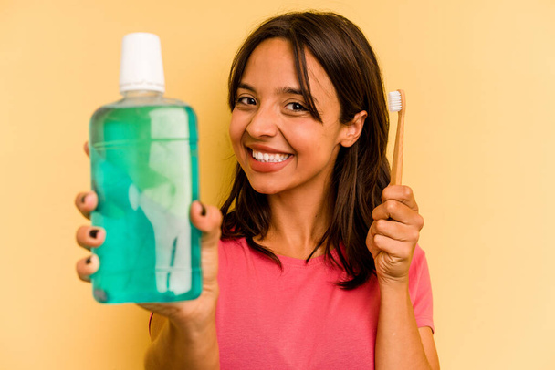 Young hispanic woman holding mouthwash isolated on yellow background - Foto, afbeelding
