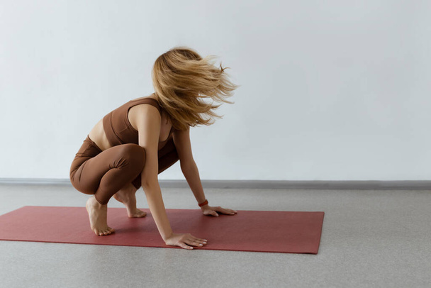 An attractive girl sits on a yoga mat. Slim body and health care.Crane Pose Bakasana. - Foto, afbeelding