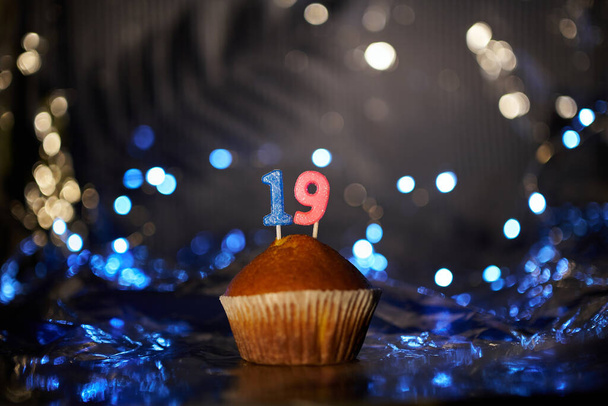 Holiday or birthday digital greeting card concept. Tasty vanilla cupcake or muffin with number 19 nineteen on aluminium foil and blurred bright background. High quality photo - Foto, immagini
