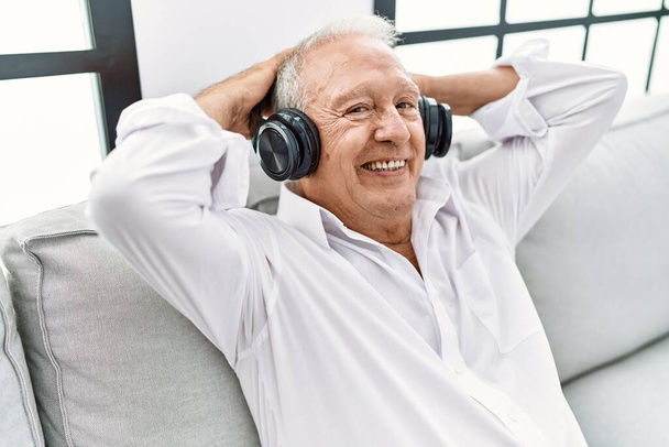 Idősebb férfi zenét hallgat otthon a kanapén ülve. - Fotó, kép