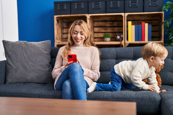 Mother and son using smartphone sitting on sofa at home - Photo, Image