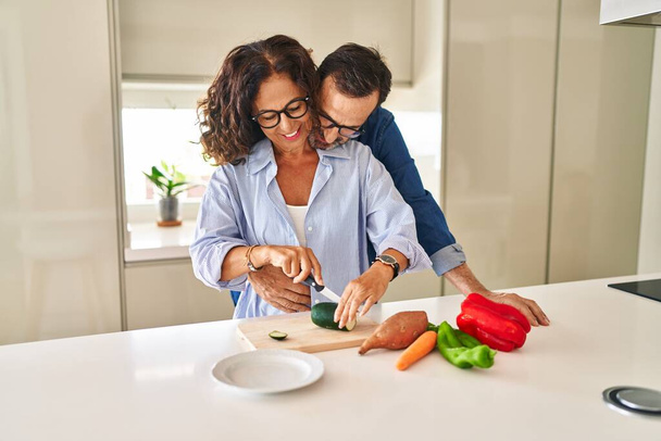Middle age hispanic couple hugging each other cooking at kitchen - Foto, Imagen