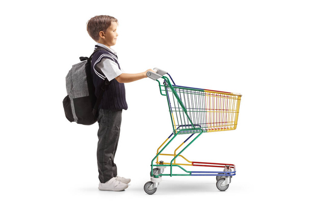 Full length profile shot of a schoolboy in a uniform with a small empty shopping cart isolated on white background - Photo, image