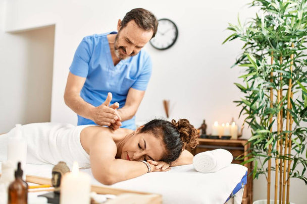Mężczyzna i kobieta w średnim wieku w mundurze terapeuty mający sesję masażu pleców w centrum urody - Zdjęcie, obraz