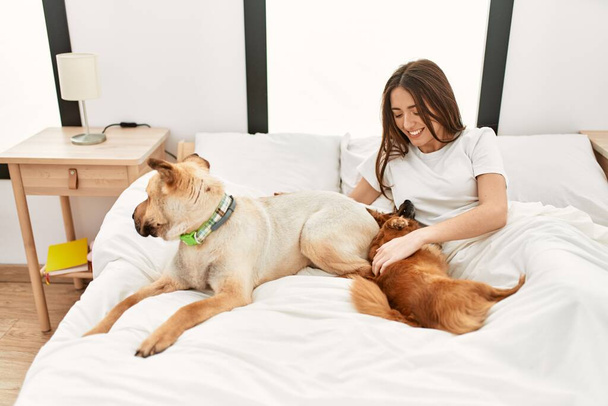 Young hispanic woman playing with dogs lying on bed at bedroom - Photo, image