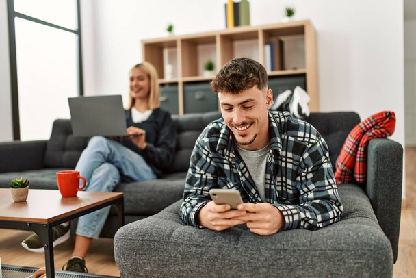Молода біла пара посміхається щаслива, використовуючи ноутбук і смартфон, сидячи на дивані вдома
. - Фото, зображення
