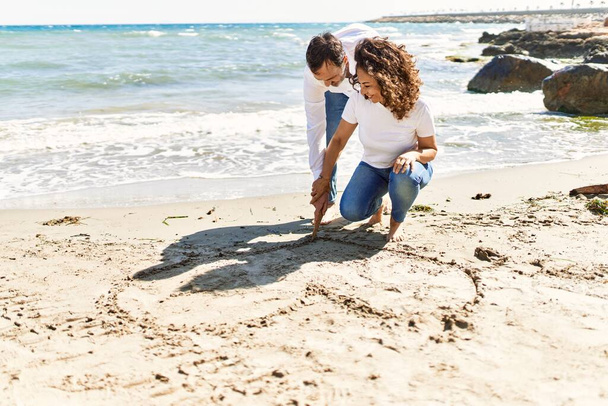 Moyen Age couple hispanique souriant heureux coeur dessin sur le sable à la plage. - Photo, image