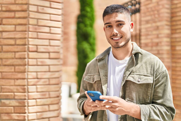 Jovem hispânico sorrindo confiante usando smartphone na rua - Foto, Imagem