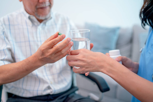 Asiatischer Senior hält Medikamentenpille in der Hand und diskutiert mit Krankenschwester oder Arzt während des Hausarztdienstes. - Foto, Bild