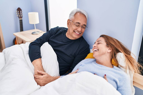 Mediana edad hombre y mujer pareja sonriendo confiado acostado en la cama en el dormitorio - Foto, imagen