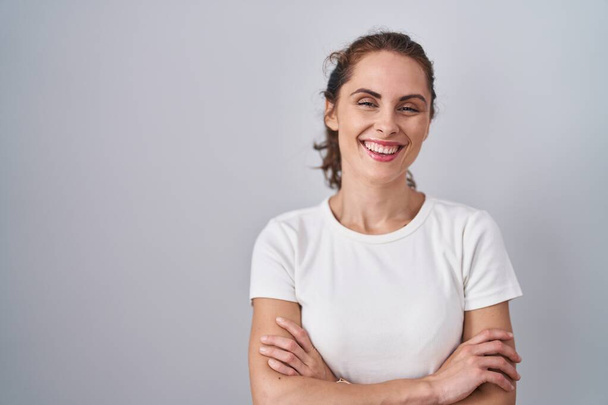 Beautiful brunette woman standing over isolated background happy face smiling with crossed arms looking at the camera. positive person.  - Foto, Imagen