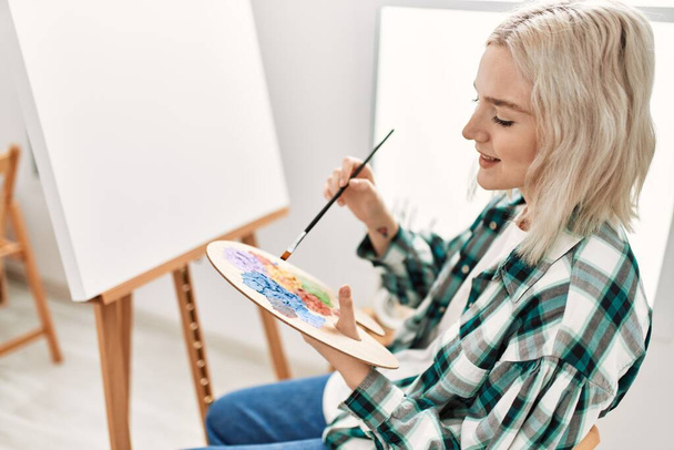 Joven estudiante artista sonriendo feliz pintura en el estudio de arte. - Foto, imagen