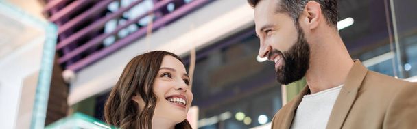 Low angle view of positive couple looking at each other in jewelry shop, banner  - Фото, изображение
