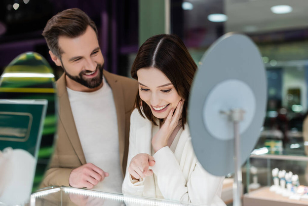 Smiling woman pointing at showcase near blurred boyfriend in jewelry shop  - Foto, Imagen
