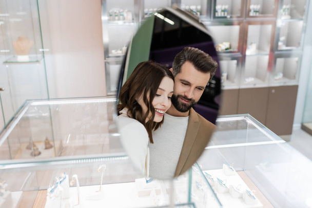 Smiling couple reflecting in mirror of jewelry shop  - Zdjęcie, obraz
