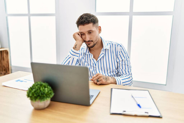 Young handsome man with beard working at the office using computer laptop thinking looking tired and bored with depression problems with crossed arms.  - Foto, Bild