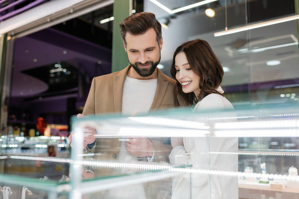 Smiling couple looking at blurred showcase in jewelry shop  - Foto, imagen