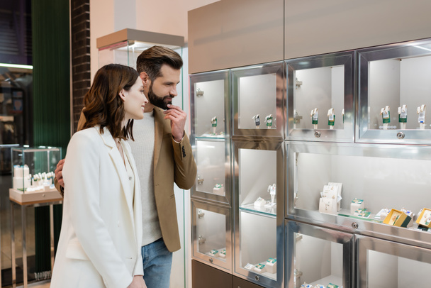 Pensive man hugging girlfriend near jewelry in shop  - Zdjęcie, obraz