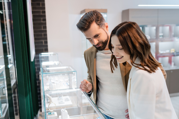 Man looking at showcase with jewelry near smiling girlfriend in store  - Photo, Image