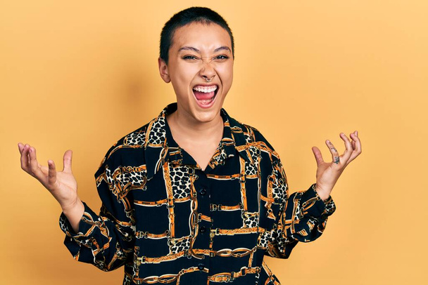 Beautiful hispanic woman with short hair wearing elegant shirt crazy and mad shouting and yelling with aggressive expression and arms raised. frustration concept.  - Foto, immagini