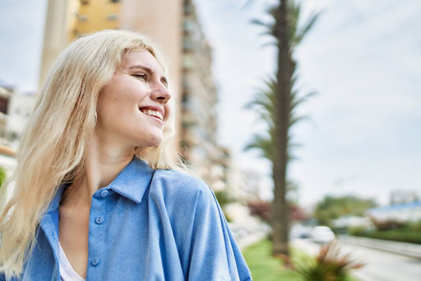 Schöne blonde junge Frau lächelt glücklich draußen an einem sonnigen Tag - Foto, Bild