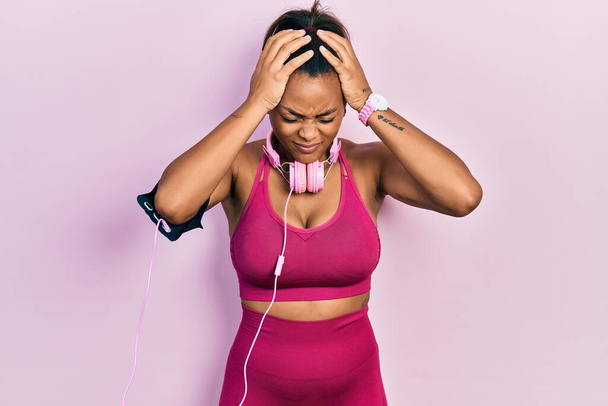Young african american girl wearing gym clothes and using headphones suffering from headache desperate and stressed because pain and migraine. hands on head.  - Foto, afbeelding
