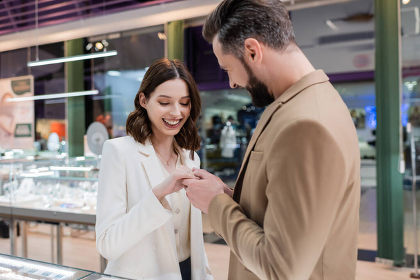 Smiling man wearing ring on hand of girlfriend in jewelry shop  - Foto, Imagen