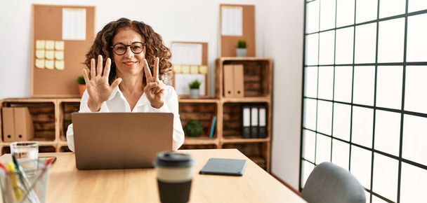 Middle age hispanic woman working at the office wearing glasses showing and pointing up with fingers number seven while smiling confident and happy.  - Φωτογραφία, εικόνα