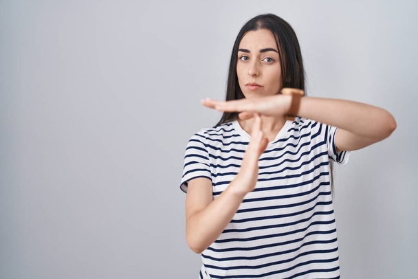 Mladá brunetka žena na sobě pruhované tričko odpykává čas gesto s rukama, frustrovaný a vážný obličej  - Fotografie, Obrázek