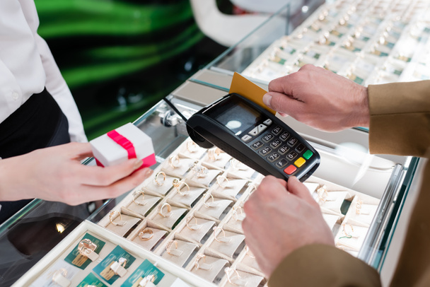 Обрезанный вид человека, платящего кредитной картой рядом с продавцом с подарочной коробкой в ювелирном магазине  - Фото, изображение