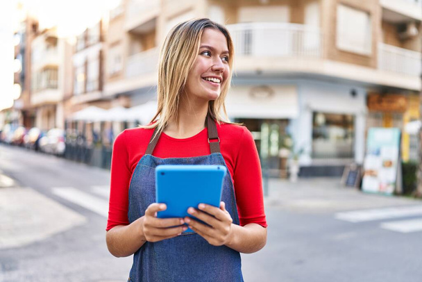 Fiatal spanyol nő bolt asszisztens használ touchpad áll az utcán - Fotó, kép